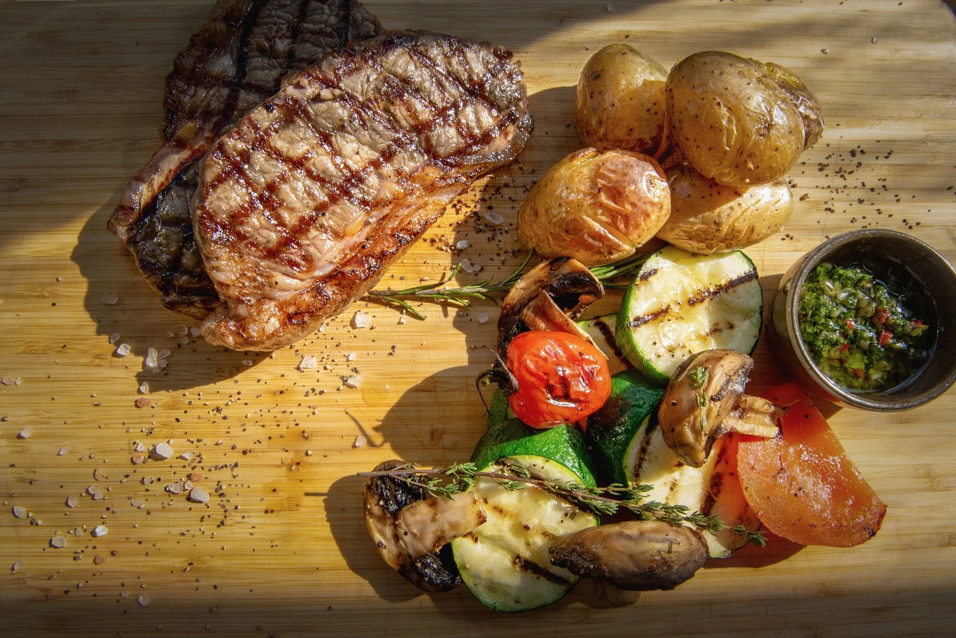 Grilintas kepsnys su keptomis bulvėmis, grilintomis daržovėmis ir žalumynų padažu